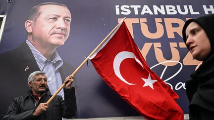 Un électeur d'Erdogan brandit un drapeau de la Turquie devant un grand poster du président sortant et candidat à l'élection présidentielle, à Istanbul, le 12 mai 2023. (OZAN KOSE / AFP)