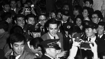 L'acteur français Alain Delon entouré de nombreux journalistes à l'aéroport Haneda de Tokyo, au Japon, le 29 mars 1963. (TATSUYA SAKAMOTO / YOMIURI via AFP)