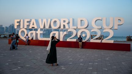 Des touristes&nbsp;prennent des photos devant un panneau de la Coupe du monde de football 2022 au Qatar, à Doha le 23 octobre 2022.&nbsp; (JEWEL SAMAD / AFP)