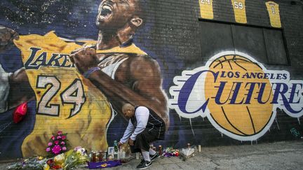 Un homme&nbsp;allume une bougie devant une peinture murale de Kobe Bryant dans le centre-ville de Los Angeles (Etats-Unis), le 26 janvier 2020. La légende de la NBA est morte ce même jour lors d'un accident d'hélicoptère. Huit autres personnes ont péri lors de cet accident, dont Gianna, sa fille de 13 ans. (APU GOMES / AFP)