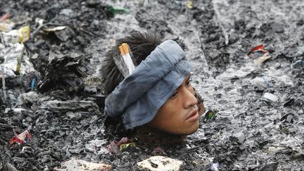 Un homme nage dans des eaux remplis de d&eacute;bris issus d'une explosion auant ras&eacute; environ 500 maisons pr&egrave;s de Manille (Philippines), le 7 avril 2011. (ERIK DE CASTRO / REUTERS)