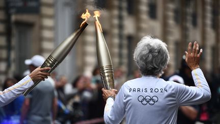 Deux porteurs de la flamme olympique se relaient à Bordeaux, le 23 mai 2024. (CHRISTOPHE ARCHAMBAULT / AFP)