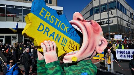 Une figure géante représentant le président russe, Vladimir Poutine, avalant une carte de l'Ukraine lors d'une manifestation contre l'invasion de l'Ukraine par la Russie, le 13 mars 2022 à Berlin. (JOHN MACDOUGALL / AFP)