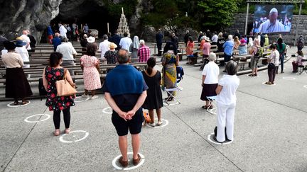 Des pélerins assistent à la retransmission d'une messe du pape François sur un écran, le 30 mai 2020 à Lourdes (Hautes-Pyrénées). (LAURENT DARD / AFP)