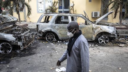 Des personnes regardent les restes de deux voitures brûlées qui appartiendrait&nbsp;à Radio Futures Media (RFM) à Dakar, au Sénégal, le 5 mars 2021. (JOHN WESSELS / AFP)