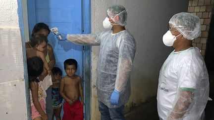 Des membres de la tribu Tikuna, dans l'Etat brésilien d'Amazonas, contrôlés par un employé du ministère de la Santé indigène à Lago Grande le 2 avril 2020 (AFP / SESAI)