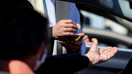 Un fidèle se saisie de l'hostie tendue par un prêtre, le 17 mai 2020 à Châlons-en-Champagne (Marne). (FRANCOIS NASCIMBENI / AFP)