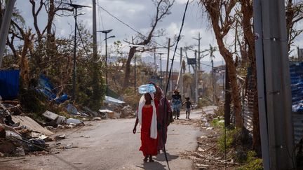 Des Mahorais se déplacent parmi les décombres et les arbres dénudés à Pamandzi, le 17 décembre 2024. Les morceaux de tôle jonchent les bords de la route. (DIMITAR DILKOFF / AFP)