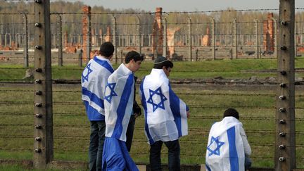 De jeunes juifs drap&eacute;s dans le drapeau isra&eacute;lien se recueillent devant les barbel&eacute;s du camp nazi d'Auschwitz-Birkenau &agrave; l'occasion de la traditionnelle "Marche des Vivants", Oswiecim (Pologne), le 19 avril 2012. (JANEK SKARZYNSKI / AFP)