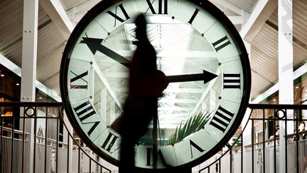 Une personne passe devant une horloge, le 25 mars 2010 au centre commercial de la Toison d'Or à Dijon. (JEFF PACHOUD / AFP)