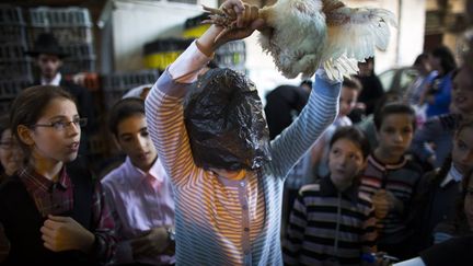 Une jeune juive ultra-orthodoxe, le visage prot&eacute;g&eacute; avec un sac plastique, fait tourner un poulet au-dessus de sa t&ecirc;te pour pratiquer le rituel de Kaparot, &agrave; J&eacute;rusalem (Isra&euml;l), le 9 septembre 2013. (RONEN ZVULUN / REUTERS)