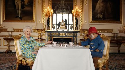 Une photo non datée de la reine Elisabeth II prenant le thé avec l'ours Paddington dans ses salons, diffusée par le palais de Buckingham, le 4 juin 2022. (BUCKINGHAM PALACE / AFP)