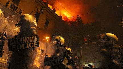 Des policiers anti-&eacute;meutes marchent pr&egrave;s d'un immeuble en flammes lors d'affrontements &agrave; Ath&egrave;nes (Gr&egrave;ce), le 12 f&eacute;vrier 2012. (PANAYIOTIS TZAMAROS / REUTERS)