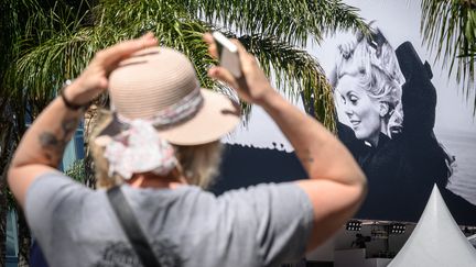 Une femme devant l'affiche officielle du 76e Festival de Cannes, le 15 mai 2023. (LOIC VENANCE / AFP)