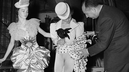 Leslie Caron observe Christian Dior qui fait d'ultimes ajustements sur le costume de Nelly Guillerm. Le couturier a réalisé les costumes pour le ballet de Roland Petit, Les treize danses.
 (ROGER-VIOLLET)