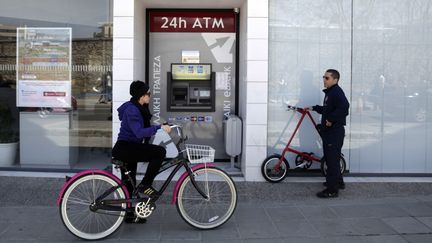 Une femme passe &agrave; v&eacute;lo devant un distributeur de la banque La&iuml;ki, dont la fermeture est envisag&eacute;e dans le plan de sauvetage europ&eacute;en, le 25 mars 2013 &agrave; Nicosie (Chypre). (YIANNIS KOURTOGLOU / AFP)