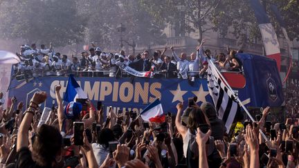 Les joueurs et le staff de l'équipe de France saluent la foule depuis un bus descendant l'avenue des Champs-Elysées, le 16 juillet 2018 à Paris. (LUCAS BARIOULET / AFP)