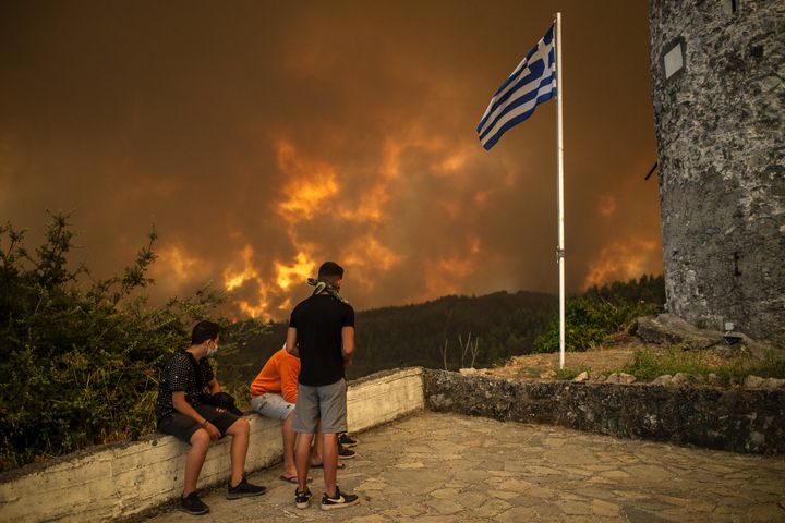 Les résidents locaux regardent l'incendie de forêt s'approchant du village de Gouves, sur l'île d'Eubée (Grèce), le 8 août 2021. (ANGELOS TZORTZINIS / AFP)