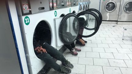 De jeunes hommes&nbsp;assis dans les machines d'une laverie du quartier de la Goutte-d'Or, dans le 18e arrondissement de Paris, le 20 décembre 2017. (@infernale75 / FRANCEINFO)