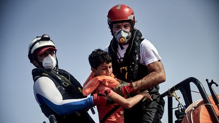 Des sauveteurs de SOS Méditerranée aidant un enfant migrant à monter à bord de leur canot de sauvetage le 1er juillet 2021. (ANTONIN BURAT / LE PICTORIUM / MAXPPP)