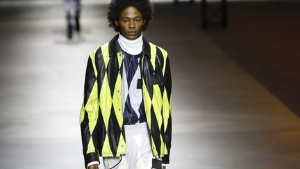 Chez Kenzo, dernier défilé de la Fashion week masculine, le show est installé dans un grand hangar. Les backstages sont sous le nez des journalistes et acheteurs. Les coulisses -maquillage, couturière, photographe et mannequins- tiennent lieu de décors. La collection Co-ed, qui s'inspire du surf en zone arctique, conjugue protection contre les éléments et sensibilité urbaine. Couleurs vives, imprimés tigrés géométriques, carreaux et motifs losanges, fleurs hawaïennes côtoient des thèmes végétaux arctiques 
 (PATRICK KOVARIK / AFP)