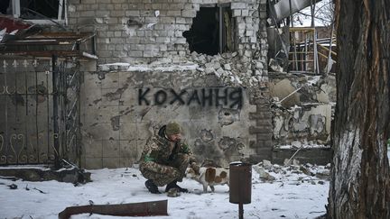 Un soldat ukrainien caresse un chien à Bakhmout (Ukraine), le 14 février 2023, devant un tag en ukrainien qui signifie "amour". (LIBKOS / AP)