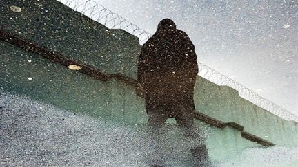 Reflet dans une flaque d'eau d'une personne longeant l'enceinte de la prison de Borgo en Haute-Corse - 07/03/2003 (AFP Photos)