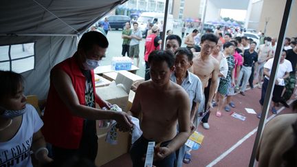 Des habitants de Tianjin (Chine), &eacute;vacu&eacute;s de leur domicile apr&egrave;s de puissantes explosions sur un site industriel,&nbsp;font la queue &agrave; l'entr&eacute;e d'une tente pour obtenir des produits de premi&egrave;re n&eacute;cessit&eacute;, jeudi 13 ao&ucirc;t 2015. (CAI YANG / AFP)