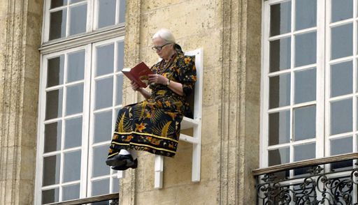 Une femme lit un livre sur une chaise accrochée à la façade d'un immeuble, le 1er avril 2004, à Bordeaux, dans le cadre d'une performance de la chorégraphe allemande Angie Hiesl, intitulée «x-times people chair». (AFP - MICHEL GANGNE)