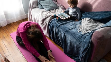 Une femme fait des exercices de pilates et stretching sur un tapis en suivant un cours sur internet. (RICCARDO MILANI / HANS LUCAS)