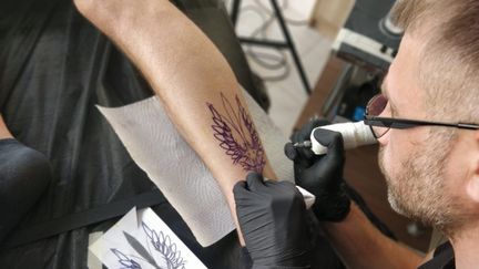 Vassil réalise un tatouage en forme de trident sur le mollet d'un client, Kiev, le 3 juin 2022. (ERIC AUDRA / RADIO FRANCE)