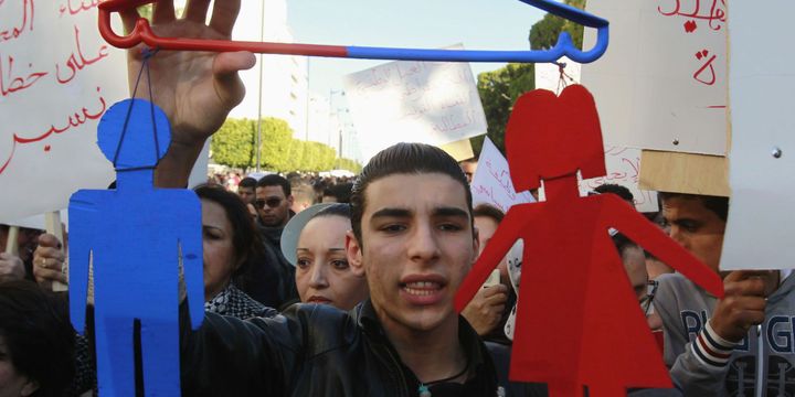 Un Tunisien tenant un symbole d'une homme et d'une femme accrochés à un ceintre pour symboliser l'égalité entre les sexes, lors d'une manifestation le 29 janvier 2011.  ( REUTERS/Louafi Larbi)