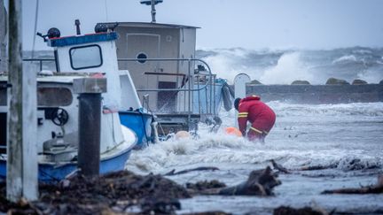 Un marin sécurise un bateau alors que les vagues s'écrasent contre la côte dans le port de Hesnaes, près de Horbelev (Danemark), le 20 octobre 2023. (INGRID RIIS / RITZAU SCANPIX / AFP)