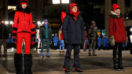 La marque de doudounes Moncler n'a pas froid aux yeux: elle l'a prouvé en présentant son défilé en plein air par des températures -24°C en ressenti. La présentation de ses collections est toujours un spectacle, et celle sur la place du Lincoln Center n'a pas dérogé à la règle, devant une petite foule de spectateurs transis: une centaine de figurants, en tenue de ski bleu roi, casque assorti, masque de ski, chaussettes et chaussures noires, ont défilé au pas militaire, se croisant en différentes figures, et faisant quelques facéties. Les mannequins, hommes et femmes, sont arrivés ensuite, certains avec des skis, d'autres un surf, d'autres encore avec un paquetage sur le dos, prenant la pose alors que de l'opéra emplissait l'espace. Les  tenues élégantes de ski, souvent coordonnées, les doudounes confortables, les grosses bottes à poils longs et toques assorties, jaunes, violettes ou bleues,  le rouge et noir d'un manteau de laine court sur mini-jupe assortie, étaient  plus que nécessaires pour résister au grand froid. Après la présentation de la marque de luxe italienne d'origine française, les spectateurs ont pris la pose avec les modèles toujours immobiles.    
 (JP Yim / GETTY IMAGES NORTH AMERICA / AFP)