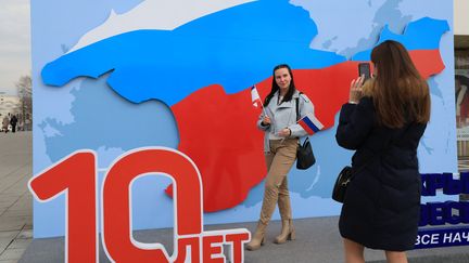 Une femme pose pour une photo devant une installation célébrant les 10 ans de l'annexion de la Crimée par la Russie, le 13 mars 2024, à Simferopol. (AFP)