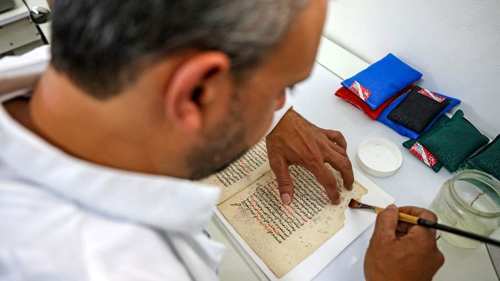 Dans son atelier où il travaille, Rami Salameh manipule avec précaution un pinceau sur un texte de grammaire arabe. (AHMAD GHARABLI / AFP)