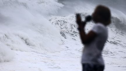 Une piétonne photographie les vagues causées par le cyclone Emnati à La Réunion, le 20 février 2022. (RICHARD BOUHET / AFP)