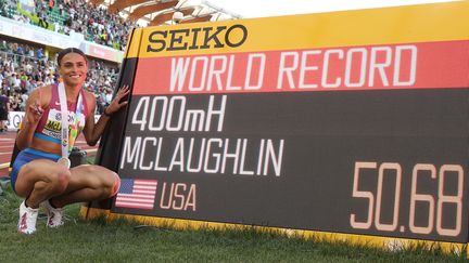 Sydney McLaughlin pose à côté du tableau d'affichage où apparaît le temps de son record du monde sur le 400 m haies, réalisé en finale des championnats du monde d'Eugene, le 22 juillet 2022. (CHRISTIAN PETERSEN / AFP)