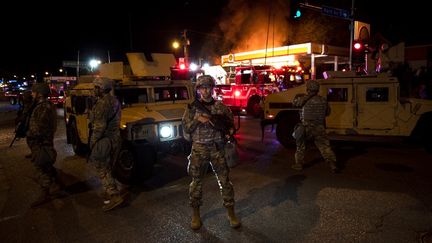 Des membres de la Garde nationale tiennent un périmètre alors qu'une équipe de pompiers s'efforce d'éteindre un incendie dans une station-service de Lake Street le 29 mai 2020 à Minneapolis, dans le Minnesota. (STEPHEN MATUREN / GETTY IMAGES NORTH AMERICA / AFP)