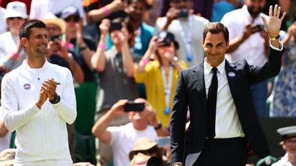 Roger Federer salue le public, au côté de Novak Djokovic, le 3 juillet 2022 lors d'une cérémonie sur le Centre Court de Wimbledon (Royaume-Uni). (ADRIAN DENNIS / AFP)