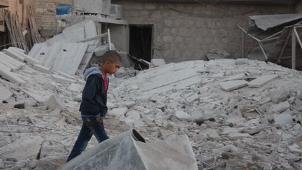 Un garçon marche au milieu des débris des immeubles d'Alep, après les raids du régime syrien et de son allié russe, le 25 septembre 2016, en Syrie.&nbsp; (AHMED HASAN UBEYD / ANADOLU AGENCY / AFP)