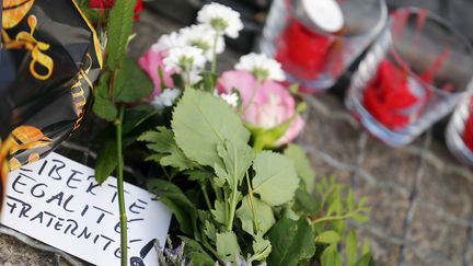 Pas de drapeau tricolore mais la devise de la France inscrite sur une carte déposée au milieu de fleurs et de bougies devant l'ambassade française à Berlin (Allemagne). (HANNIBAL HANSCHKE / REUTERS)