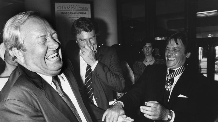 Jean-Marie Le Pen et Alain Delon hilares lors de la cérémonie faisant de l'acteur un commandeur des Arts et des Lettres, le 26 mai 1986 au théâtre des Champs-Elysées, à Paris. (FREDERIC REGLAIN / GAMMA-RAPHO / GETTY IMAGES)