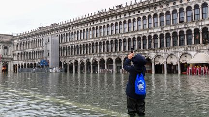 Un touriste prend une photo de la place Saint-Marc inondée, le 24 novembre 2019 à Venise (Italie). (MIGUEL MEDINA / AFP)