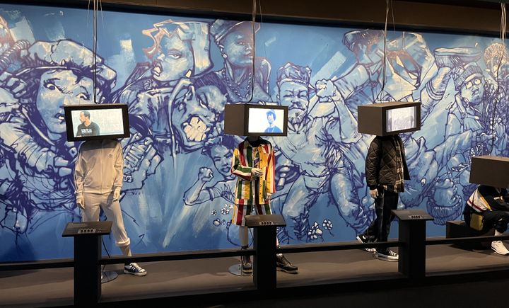 La fresque bleue réalisée spécialement à l'exposition par la légende Mode 2.&nbsp;Au premier plan,&nbsp;des mannequins à têtes d'écrans montrent les différents styles de danse et les tenues&nbsp;afférentes des B-Boys. (LAURE NARLIAN / FRANCEINFO)