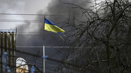 Un drapeau ukrainien déchiré flotte dans un quartier de Kiev,&nbsp;à quelques mètres d'un&nbsp;entrepôt bombardé, le 4 mars 2022. (ARIS MESSINIS / AFP)