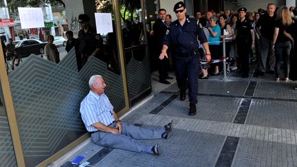 Un retrait&eacute; pleure assis sur le sol devant une banque, &agrave; Thessalonique, en Gr&egrave;ce.&nbsp; (SAKIS MITROLIDIS / AFP)