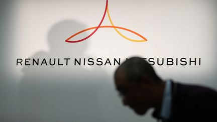 Un membre des médias défile devant un nouveau logo montrant Renault, Nissan et Mitsubishi avant une conférence de presse au siège de Nissan à Yokohama, dans la préfecture de Kanagawa, le 12 mars 2019. (BEHROUZ MEHRI / AFP)