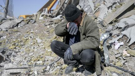 Un homme aide des soldats ukrainiens à chercher des corps dans les débris de l'école militaire touchée par des roquettes russes, à Mykolaiv, dans le sud de l'Ukraine, le 19 mars 2022. (BULENT KILIC / AFP)