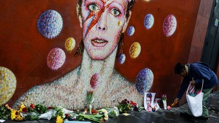 Des fleurs déposées au pied d'un mur à l'effigie de David Bowie à Londres (Royaume-Uni), le 11 janvier 2016. (CHRIS RATCLIFFE / AFP)